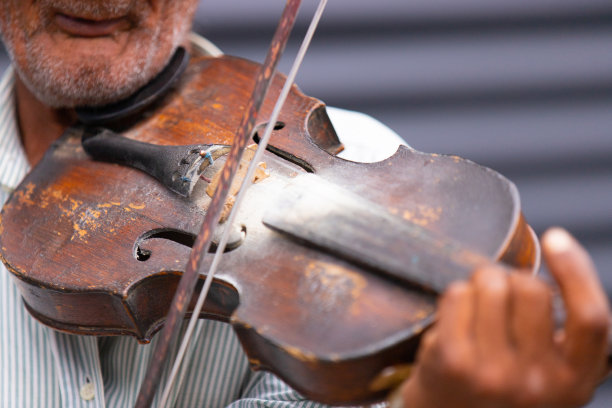 一位满脸皱纹的老人在街上演奏着古典音乐，小提琴和小提琴弓的特写照片。图片下载