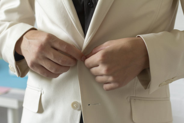 年轻人正在穿衣服。时尚服装的概念是一个男人穿衣服并扣上白色夹克的特写镜头。图片下载