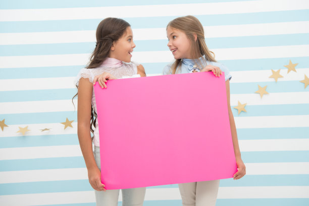 女孩举着公告横幅。女孩们举着纸横幅宣布。孩子们高兴地在空白的纸上抄写公告。孩子们宣布的概念。神奇的令人惊讶的新闻图片下载