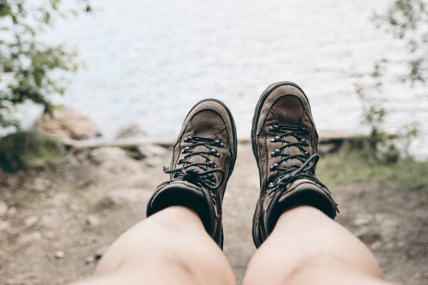 一个女人的腿和旧皮靴的特写。模糊的湖泊，河流和灌木背景。夏季户外，远足的概念。有选择性的重点。自然生活的照片。前视图。图片下载