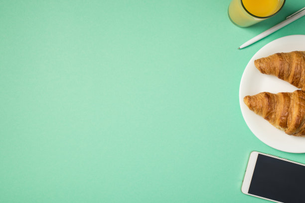 顶视图照片的果汁，笔盘与羊角面包和智能手机在孤立的绿松石背景空白图片下载