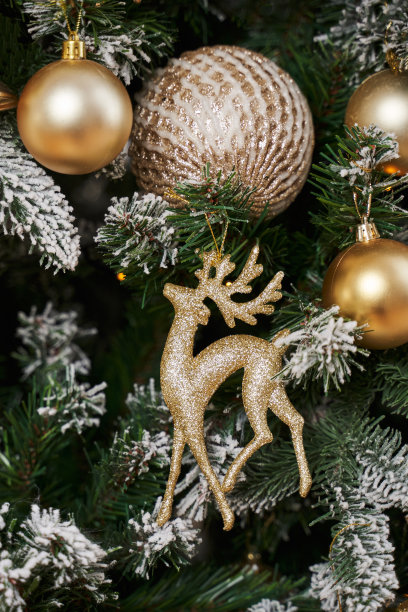 圣诞树玩具的形式金鹿和金球在冰雪覆盖的圣诞树树枝图片下载