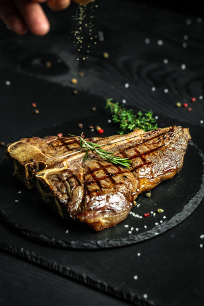 美国肉品餐厅的美味t骨牛排或陈年和牛肉排。厨师在黑色背景上撒上调味料。垂直的图像图片下载