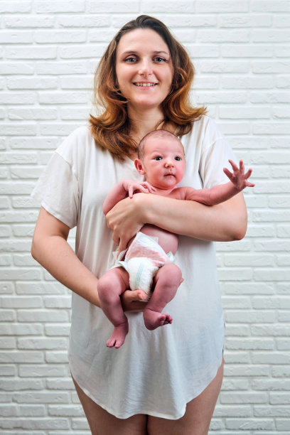 一位快乐的成年妇女抱着一个刚出生的小男孩，背景是一堵白色砖墙图片下载