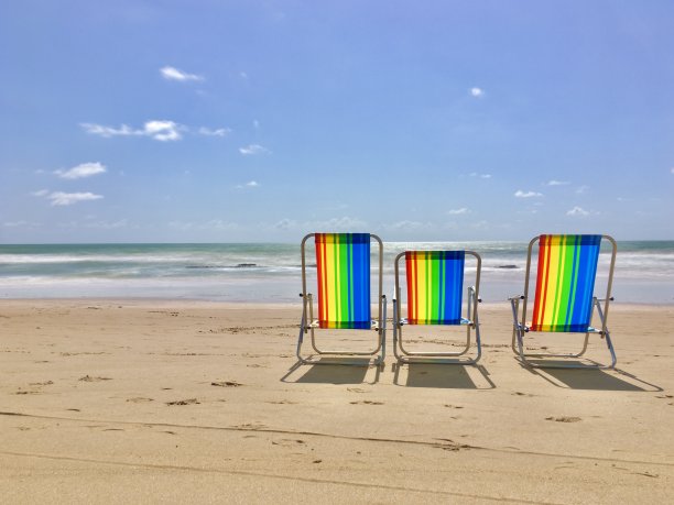 在空旷的阳光沙滩上，彩虹色的沙椅图片下载