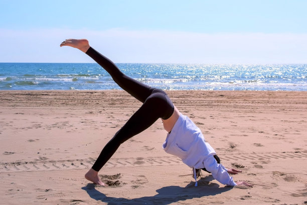 女人做下犬式瑜伽在海边沙滩运动锻炼。图片下载