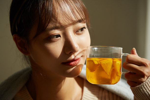 一个年轻的亚洲女人在家里喝水果茶放松图片下载