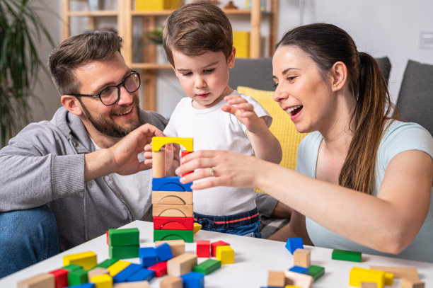 年轻的幸福的家庭。妈妈和爸爸在家里和她可爱的蹒跚学步的儿子玩木制玩具。家庭教育图片下载