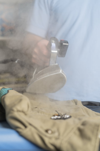 一个洗衣工人用蒸汽熨烫夹克的特写镜头图片下载