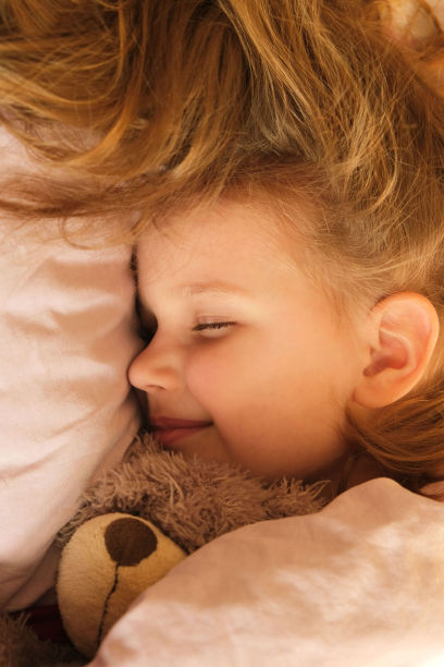 穿着睡衣微笑着睡觉的小女孩躺在床上，阳光透过窗户照进来图片下载