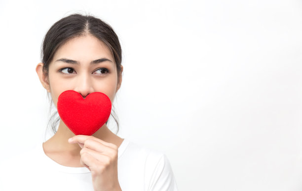 女孩的肖像手拿红纸心盖住她的脸孤立在白色背景上。特写亚洲女人与红色的心爱情人节概念图片下载