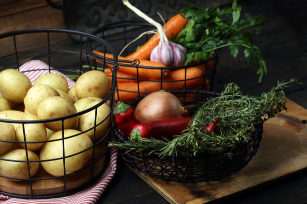 生土豆、胡萝卜、洋葱、大蒜、辣椒、百里香、迷迭香和欧芹装在金属篮子里放在桌子上图片下载