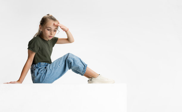 一个可爱的青少年学校白人女孩戴着眼镜坐在地板上孤立的白色工作室背景。侧视图图片下载