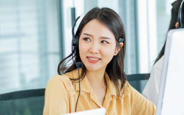 专注亚洲美女魅力女性呼叫中心愉快愉快地微笑着，戴着耳机，坐在办公室或代理处的电脑屏幕前监控，为客户提供服务。图片下载
