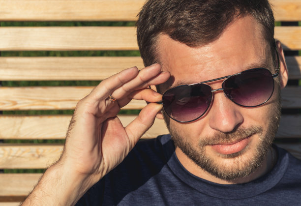 英俊的成年男子的肖像，胡茬戴着太阳镜。有魅力的男人用手拿着太阳镜。图片下载