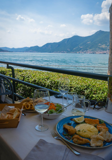 在意大利伊塞奥湖的映衬下，蓝色的盘子上放着各式各样的炸鱼、玉米粥和沙拉图片下载