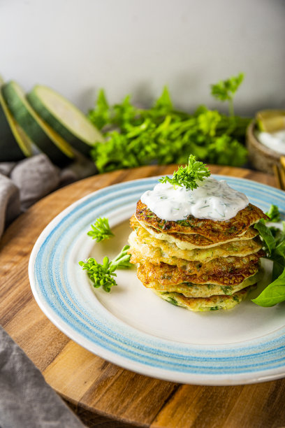 蓝色盘子上的西葫芦煎饼、香草和酸奶油特写垂直照片。素食菜图片下载
