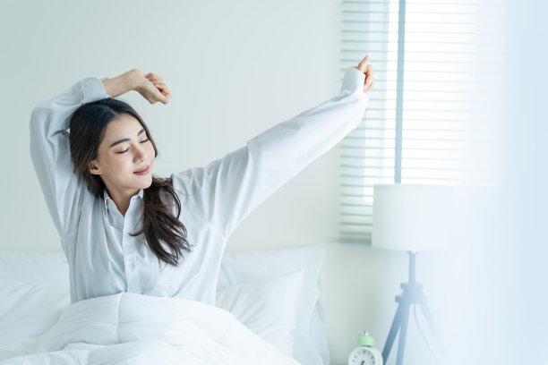 穿着睡衣的亚洲美女在幸福的早晨醒来。迷人的年轻女子微笑着，感到幸福和放松，然后在床上伸展身体后，从卧室的家。图片下载