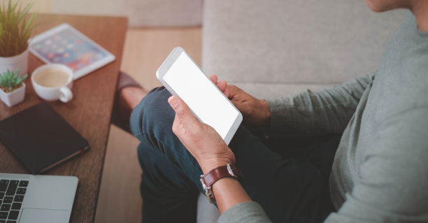 这是一个男人在办公桌旁用手拿着智能手机或手机模型的图片。图片下载