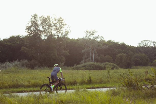 年轻的男子铁人三项运动员在开阔的道路上骑自行车。职业运动员在晴朗的夏日从事铁人三项运动图片下载