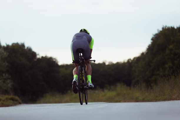 年轻的男子铁人三项运动员在开阔的道路上骑自行车。职业运动员在晴朗的夏日从事铁人三项运动图片下载