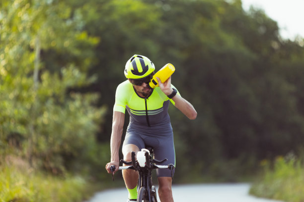 年轻的男子铁人三项运动员在开阔的道路上骑自行车。职业运动员在晴朗的夏日从事铁人三项运动图片下载