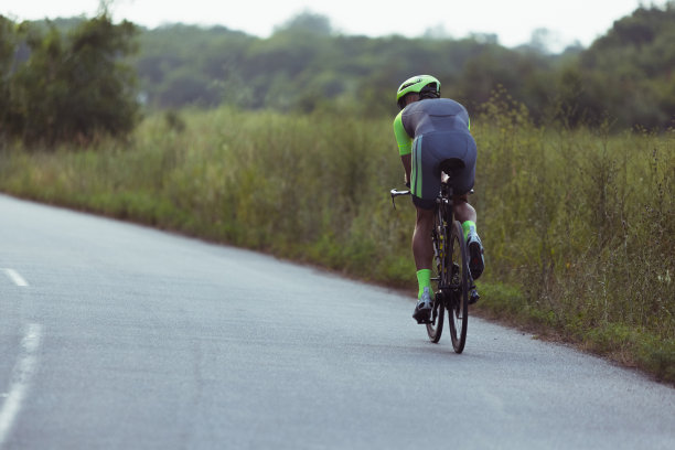 年轻的男子铁人三项运动员在开阔的道路上骑自行车。职业运动员在晴朗的夏日从事铁人三项运动图片下载