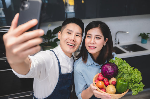 夫妻一起用手机微笑，与女友和男友站在公寓厨房的成熟的室内照片，为媒体退休的友谊拥抱图片下载