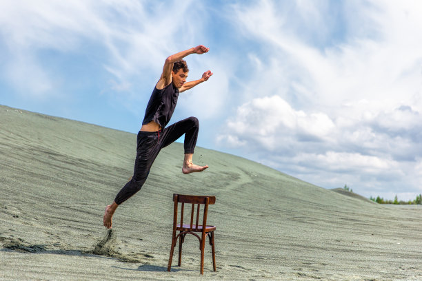 穿着运动服的年轻人在沙丘的背景下跳过木椅图片下载