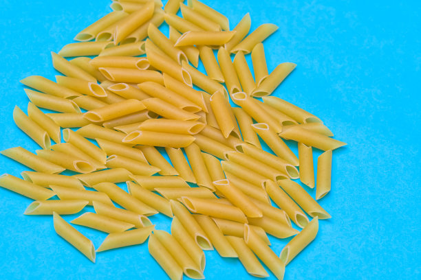 一把生的通心粉放在蓝色背景上。概念食物，烹饪和健康的生活方式图片下载