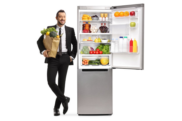 一个年轻商人的全身肖像与杂货袋靠在冰箱上图片下载
