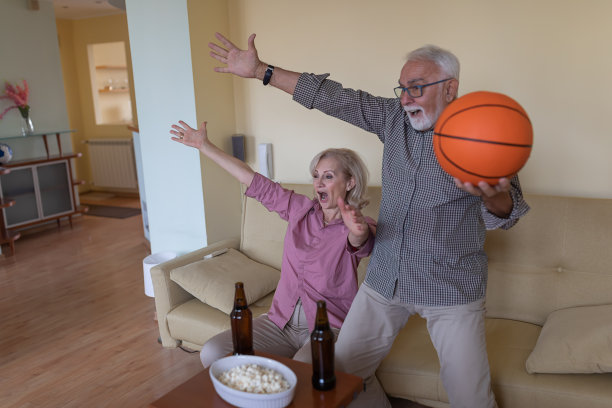 老男人和他的妻子在舒适公寓看篮球比赛。图片下载