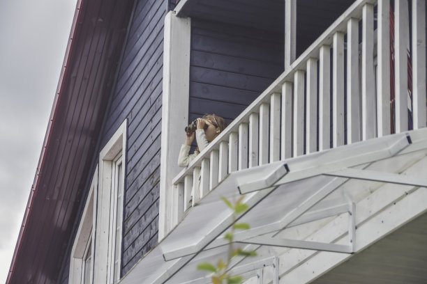 小女孩站在房子的阳台上，透过望远镜看图片下载