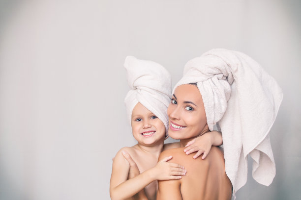 一个年轻的成年妇女和女儿在淋浴后用新鲜的毛巾拥抱在孤立的背景图片下载