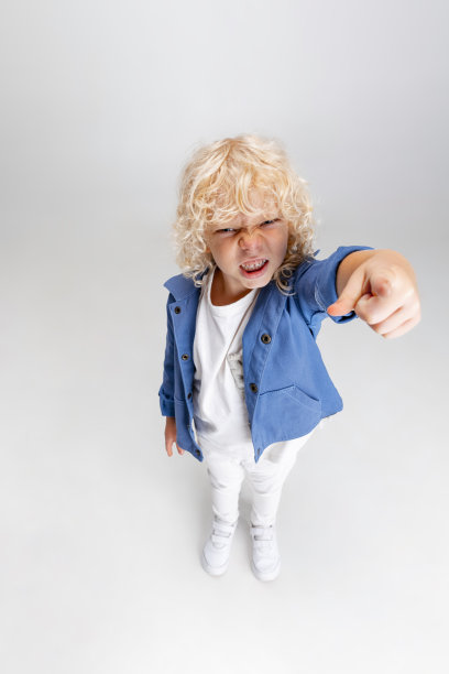 可爱的小卷发学前班男孩穿着休闲装看着相机孤立在白色的摄影棚背景。图片下载