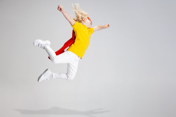 可爱的小卷发学前班男孩在红色斗篷和面具飞行隔离在白色的工作室背景。图片下载