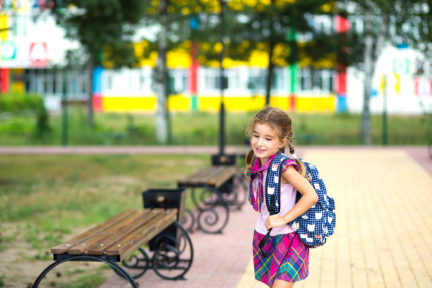 一个开朗的女孩背着书包，穿着校服在校园里。9月1日回到学校。一个快乐的学生。小学教育，小学班级。学生肖像图片下载