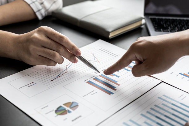 特写照片的两个商人指着一个图表格式的销售数据表，他们正在开会的主题管理销售增长。商务合作和销售管理的理念。图片下载