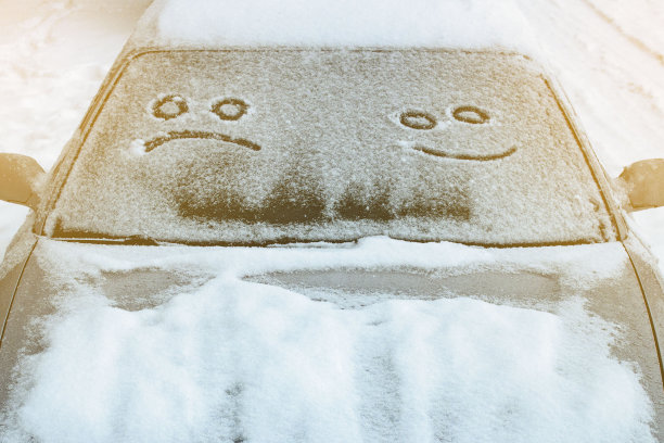 一辆汽车挡风玻璃上的第一场雪里画着一张又悲又喜的脸，以笑脸的形式出现。前景和背景模糊与散景效果图片下载