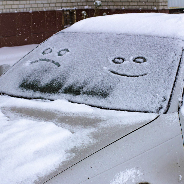 一辆汽车挡风玻璃上的第一场雪里画着一张又悲又喜的脸，以笑脸的形式出现。前景和背景模糊与散景效果图片下载