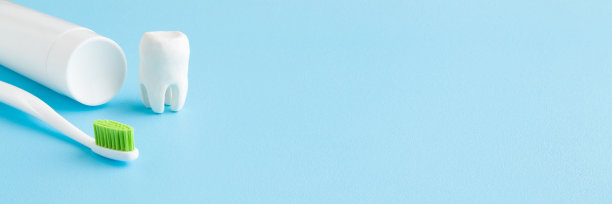 白色的牙齿，一管牙膏，绿色刷毛的牙刷在浅蓝色的桌子背景上。柔和的颜色。特写镜头。人们牙齿卫生观念。空出文本或标志的位置。牙科宽横幅。图片下载