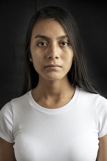 一个庄重而美丽的黑头发拉丁裔女子，身穿白色t恤，黑色背景的垂直中特写镜头。图片下载