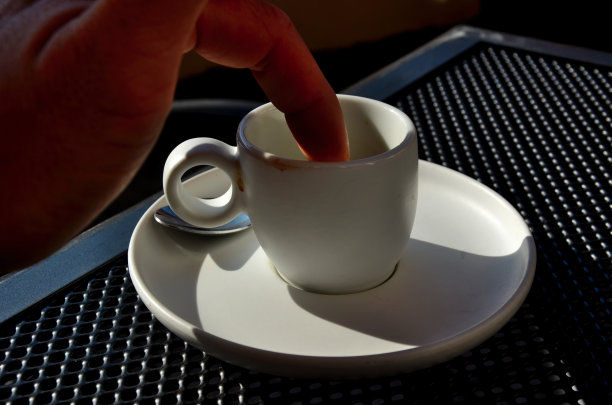 一名男子试图用手指从白色瓷杯上去除一只苍蝇或灰尘。他往里面看了看，看到了底部，剩下的糖和咖啡都在那里。咖啡馆里的线框桌子图片下载