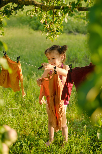 一个小女孩在大自然中把洗过的衣服挂在晾衣绳上晾干图片下载