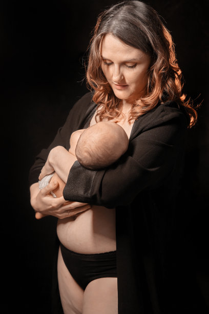 快乐的母亲抱着一个熟睡的新生男婴，黑色的背景。妈妈微笑着，手里抱着一个孩子图片下载