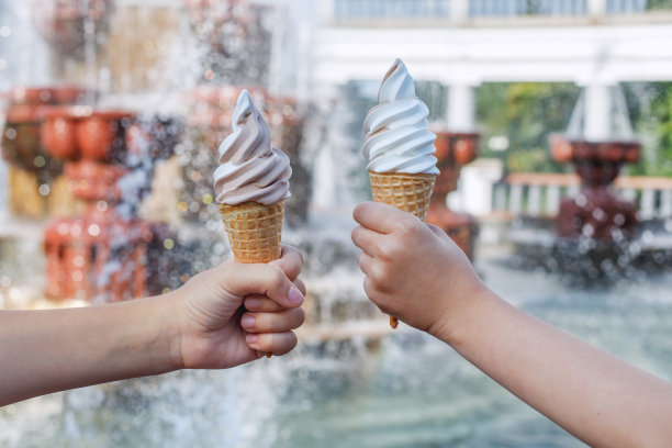 在喷泉的背景下，孩子们手里拿着两个甜筒和奶油冰淇淋。图片下载