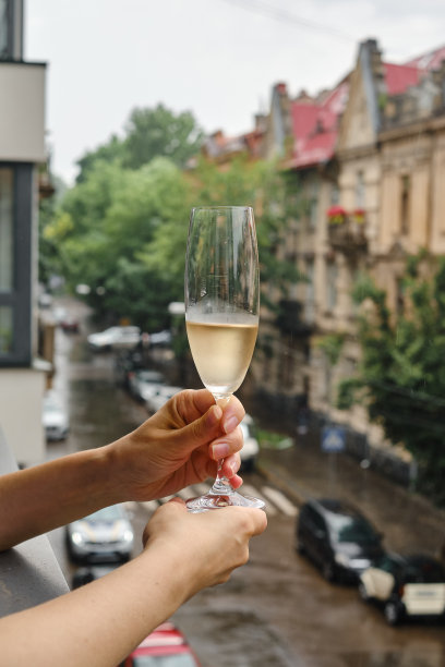 阳台上拿着酒杯的女孩。喝点白葡萄酒，享受这一刻。独自庆祝节日。轻松的生活方式。快乐的女人下班后休息。美丽的欧洲庭院图片下载