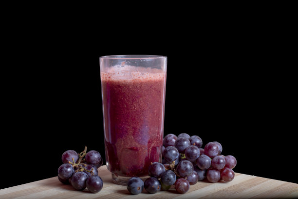 新鲜的葡萄汁，黑色和红色的葡萄放在木桌上，背景是黑色的图片下载