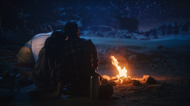 幸福的夫妇在峡谷露营，坐在一起看篝火和星空，她休息她的头在他的肩膀。两个旅行的人在鼓舞人心的假期旅行惊奇于银河之星图片下载