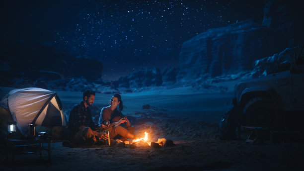 快乐的情侣在峡谷露营，坐在一起看篝火，聊天，看夜空。两个旅行中的年轻人在鼓舞人心的假期旅行中惊叹于银河之星图片下载